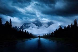Figure standing on a road toward misty mountains at dusk