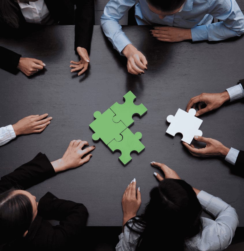 Hands connecting puzzle pieces around a table
